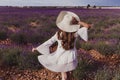 Charming Young woman with a hat and white dress in a purple lavender field at sunset. LIfestyle outdoors. Back view Royalty Free Stock Photo