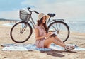 Young woman holds a book and looking at camera while sitting on the beach. Royalty Free Stock Photo