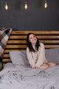 charming young woman in knitted beige sweater in bed with grey linens. modern loft bedroom in brown and gray colors