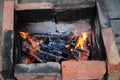 Smoldering cracked firewood with orange color flames among ashes. Terracotta red and smoky black charred bricks