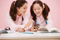 Chatty twin schoolgirls sitting behind schooldesk, looking at smartphone