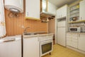 Cheap kitchen with white furniture and yellow details, broken appliances and stoneware floors