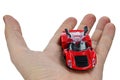 Cheap red plastic model of street-legal vintage racing car with opened gullwing doors, held in left palm of adult man, white backg Royalty Free Stock Photo