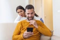 Cheater man dating on line with a smart phone and girlfriend is spying sitting on a sofa at home Royalty Free Stock Photo