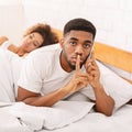 Cheating african husband talking privately on cellphone in family bed Royalty Free Stock Photo