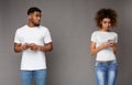 Sad black man looking at his girlfriend, focused woman texting on phone