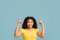 Check this. Cheerful african american lady looking and pointing fingers up, standing on blue background with copy space Royalty Free Stock Photo