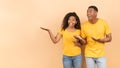 Check this. Excited african american couple demonstrating free copy space, peach studio background, panorama, banner