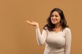 Check this offer. Positive arab lady holding her open palm, demonstrating invisible object, beige background, free space