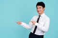 Check it. Portrait of young smiling asian man standing on light blue isolated background and pointing with his index fingers aside Royalty Free Stock Photo