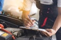 check up and car service shop concept. Mechanic writing job checklist to clipboard to estimate repair quotation to client at Royalty Free Stock Photo