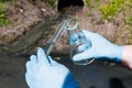 Hand in a glove with a bulb and a test tube against the background of a sewer pipe, dirty water. Royalty Free Stock Photo