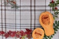 checkered beige autumn background with edible cut pumpkin and crimson yellow leaves