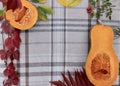 checkered beige autumn background with edible cut pumpkin and crimson yellow leaves