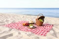 Checkered blanket with picnic basket and products on sunny beach. Royalty Free Stock Photo