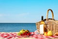 Checkered blanket with picnic basket and products on sunny beach. Space for Royalty Free Stock Photo