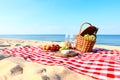 Checkered blanket with picnic basket and products on sunny beach. Space for Royalty Free Stock Photo