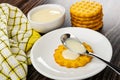 Napkin, bowl with condensed milk, stack of cookies, spoon with condensed milk on cookie in saucer on wooden table Royalty Free Stock Photo