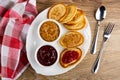 Napkin, bowls with raspberry jam, peanut butter, pancakes with jam and peanut butter in dish, fork, spoon on table. Top view