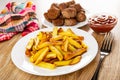 Napkin, fried meatballs in plate, ketchup in bowl, pieces of fried potato in plate, fork on wooden table