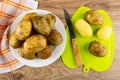 Napkin, raw potatoes in plate, unpeeled potatoes, knife, peeled potato on cutting board on wooden table. Top view