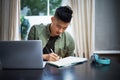 Checking back to his design brief. a handsome young man taking notes while working on his laptop at home.