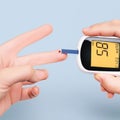 Checking blood sugar level with a glucometer on blue background Royalty Free Stock Photo