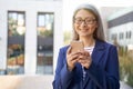 Checking email. Portrait of cheerful mature business woman in classic wear using smartphone and smiling while standing Royalty Free Stock Photo