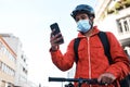 Checking the route to his delivery address. a masked man using his cellphone while out on his bicycle for a delivery.