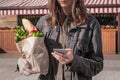 Checking shopping list in smarphone while shopping for food. Attractive young woman in casual style clothes holding Recyclable pa Royalty Free Stock Photo