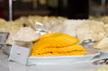 Cheddar cheese slices on white plate, different blurred other kind of cheese on background