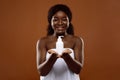 Cheeful Black Woman With Bottle Of Moisturising Body Lotion Over Brown Background Royalty Free Stock Photo