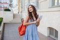 Cheeful woman with backpack and book walking in the city