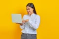 Cheeful young Asian woman holding and using laptop isolated over yellow background