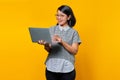 Cheeful young Asian woman holding and using laptop isolated over yellow background