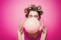 Cheeky girl with bubble gum posing on pink background in body, with curlers on head. Pretty woman with sweet makeup making Royalty Free Stock Photo