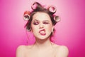 Cheeky girl posing on pink background in body, with curlers on head. Pretty woman with sweet makeup in studio