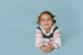 Cheeky little girl in striped sweater lying on the floor over blue background Royalty Free Stock Photo