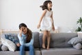 Tired mother has headache little daughter jumping on couch
