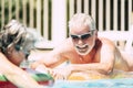 Cheerful and active lifestyle old senior couple enjoy the summer sun together at the pool with coloured lilos - aged retired Royalty Free Stock Photo
