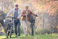 Cheerful active senior couple with bicycles walking through park together