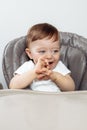 Cheerful adorable baby boy laughing with finger in his mouth sitting in high chair. Royalty Free Stock Photo