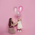 Cheerful adorable mother and daughter with pink ballon on pink studio background. Portrait of young mom and cute child baby girl Royalty Free Stock Photo