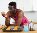 Cheerful naked man in red apron tasting muffin in home kitchen Royalty Free Stock Photo