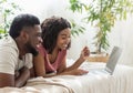 Cheerful black couple using laptop, lying on bed Royalty Free Stock Photo