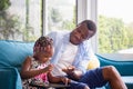 Cheerful african american father and daughter playing in living room, Cute little girl sitting on the sofa and playing on tablet Royalty Free Stock Photo