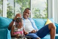 Cheerful african american father and daughter playing in living room, Cute little girl sitting on the sofa and playing on tablet Royalty Free Stock Photo