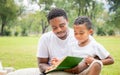 Cheerful african american father and son reading a book, Happy dad and son having a picnic in the park, Happiness family concepts Royalty Free Stock Photo