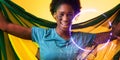 Cheerful african american female fan with brazilian flag and face paint by circle and plants Royalty Free Stock Photo