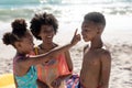 Cheerful african american girl applying suntan lotion on brother's nose by mother at beach Royalty Free Stock Photo